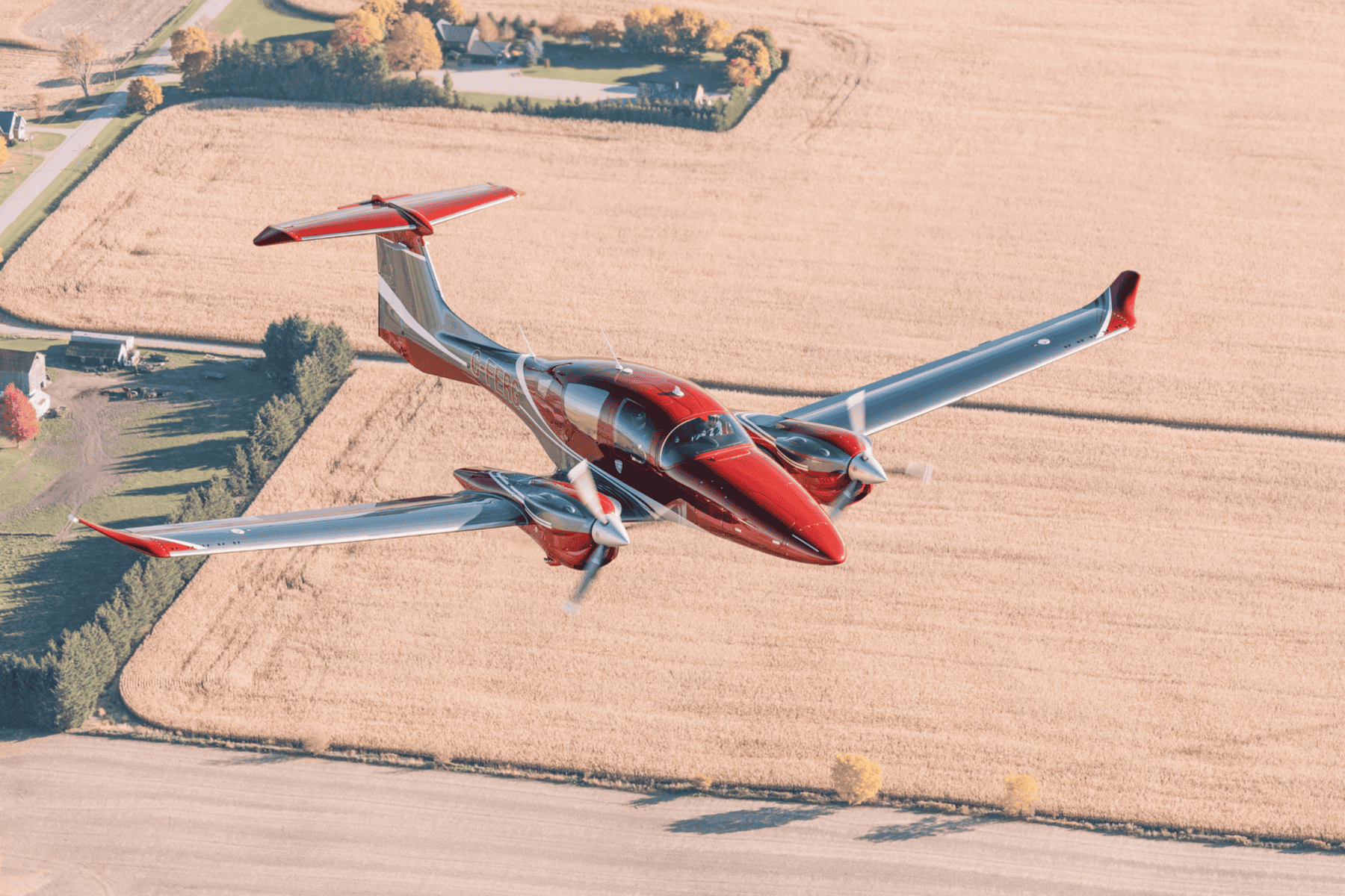 Red aircraft flying over a rural landscape