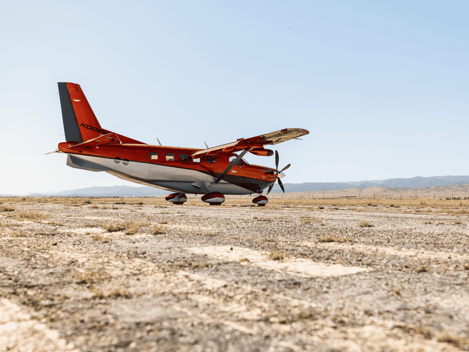 Red airplane parked on dry desert airfield.