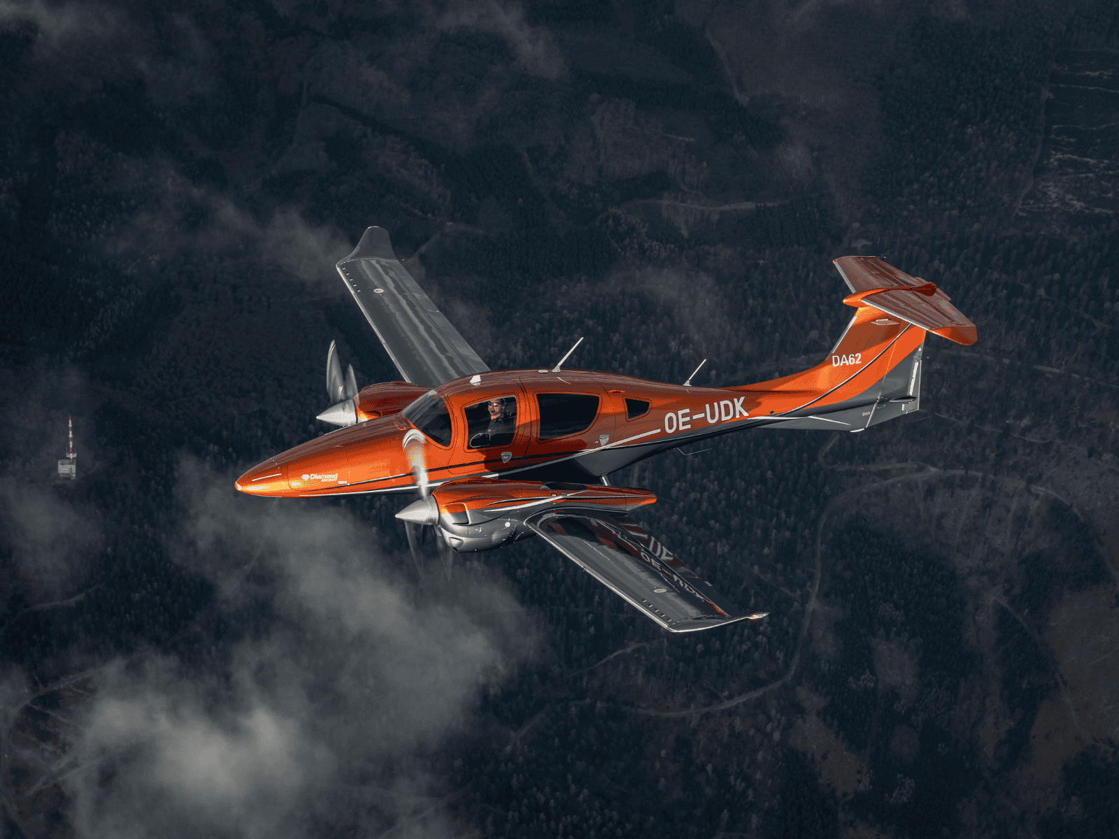 Orange twin-engine airplane flying above forest.