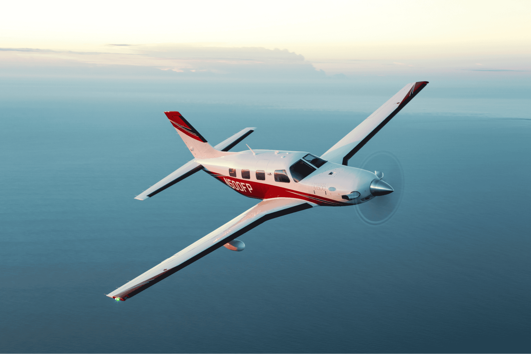 Small airplane flying over ocean at sunset.