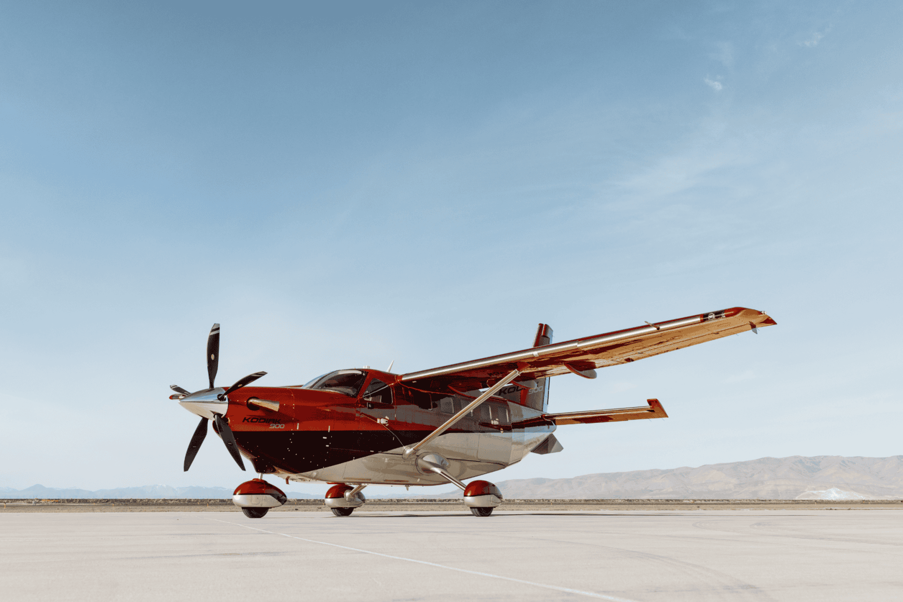 Red propeller plane on tarmac, blue sky background.
