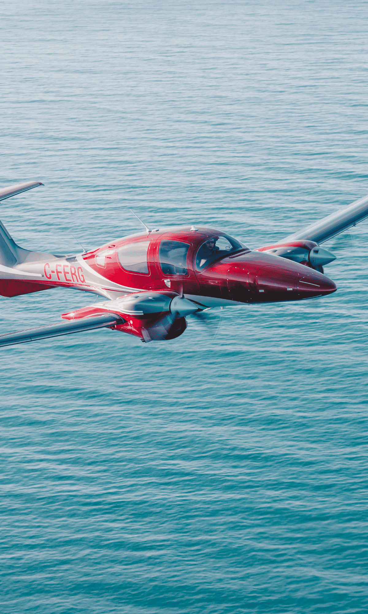 Red and silver airplane flying over the ocean.