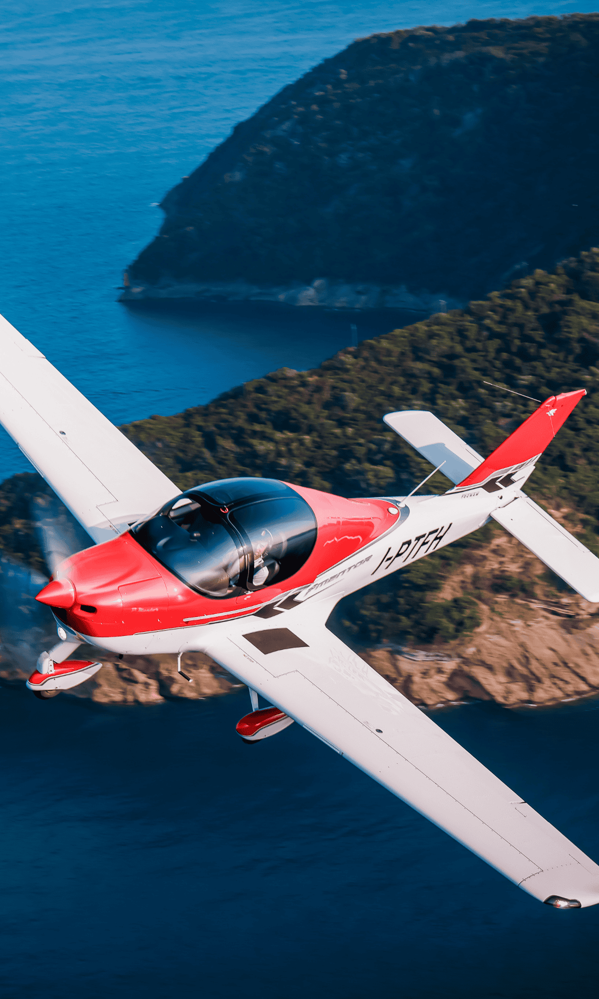 Red and white airplane flying over a coastline.
