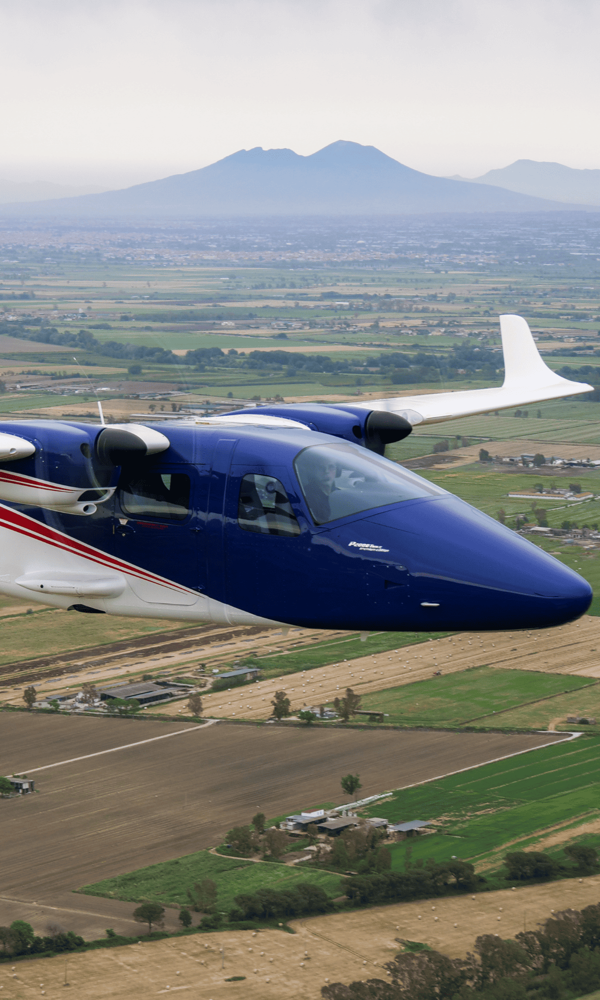 Blue aircraft flying over green fields