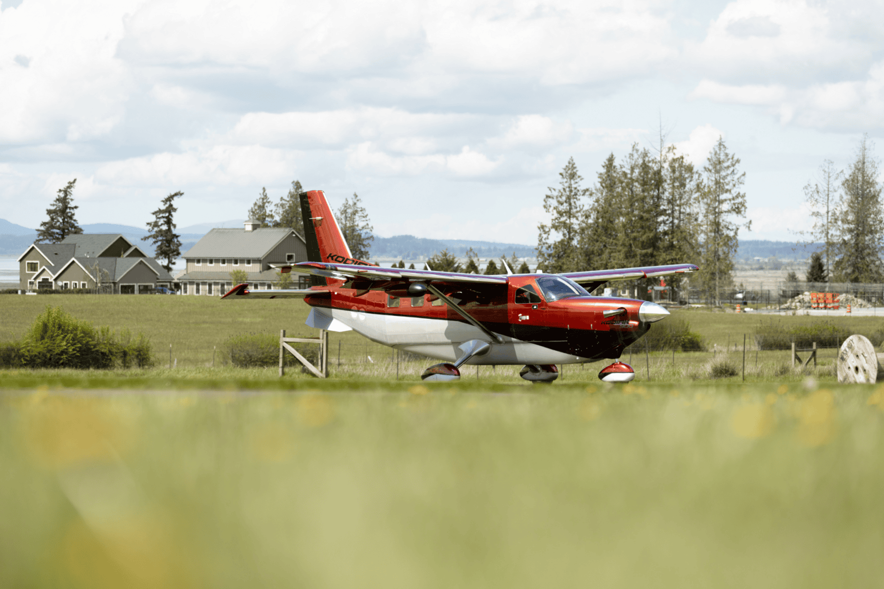 Red plane on grass, houses in background.