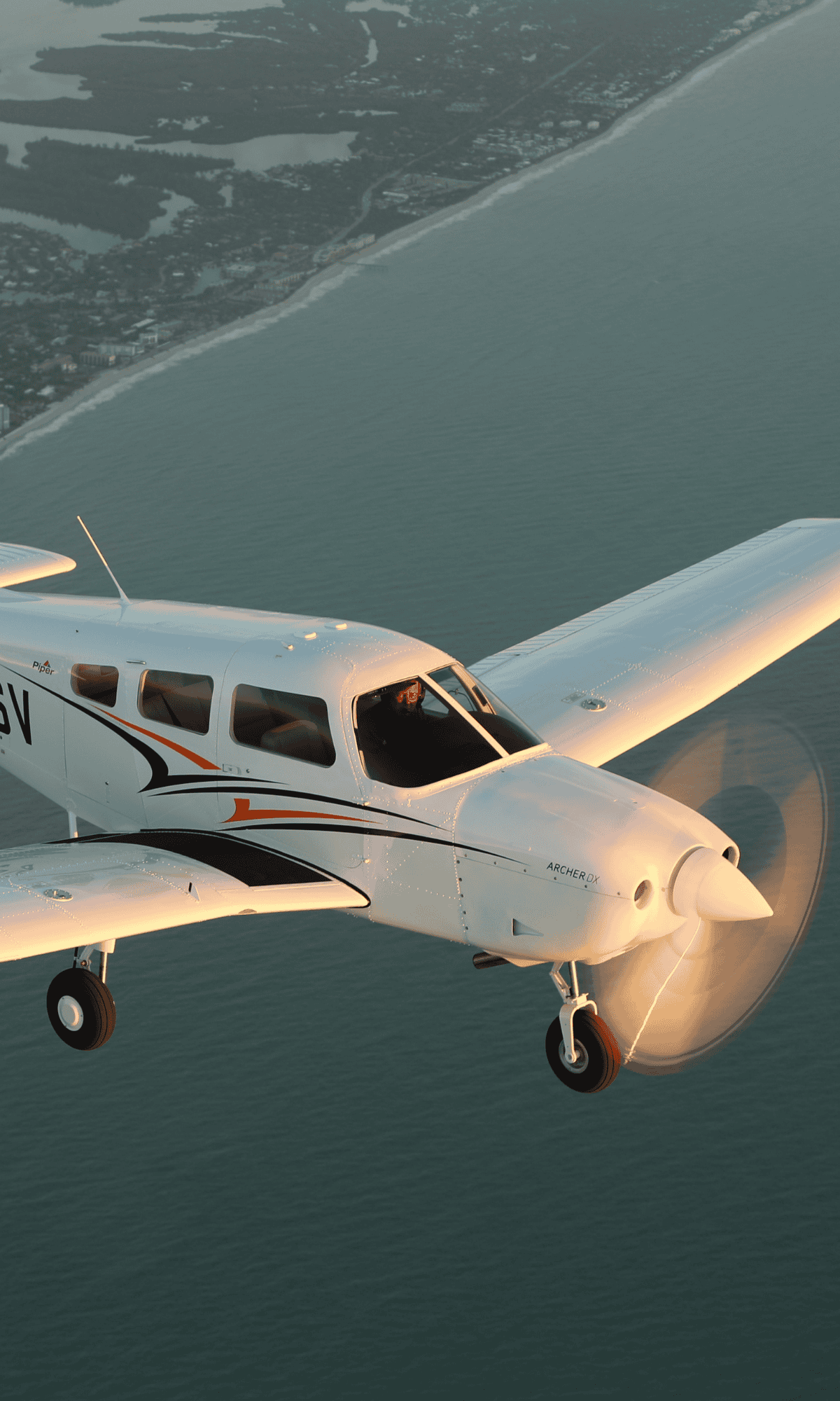 Small airplane flying over coastline at sunset.