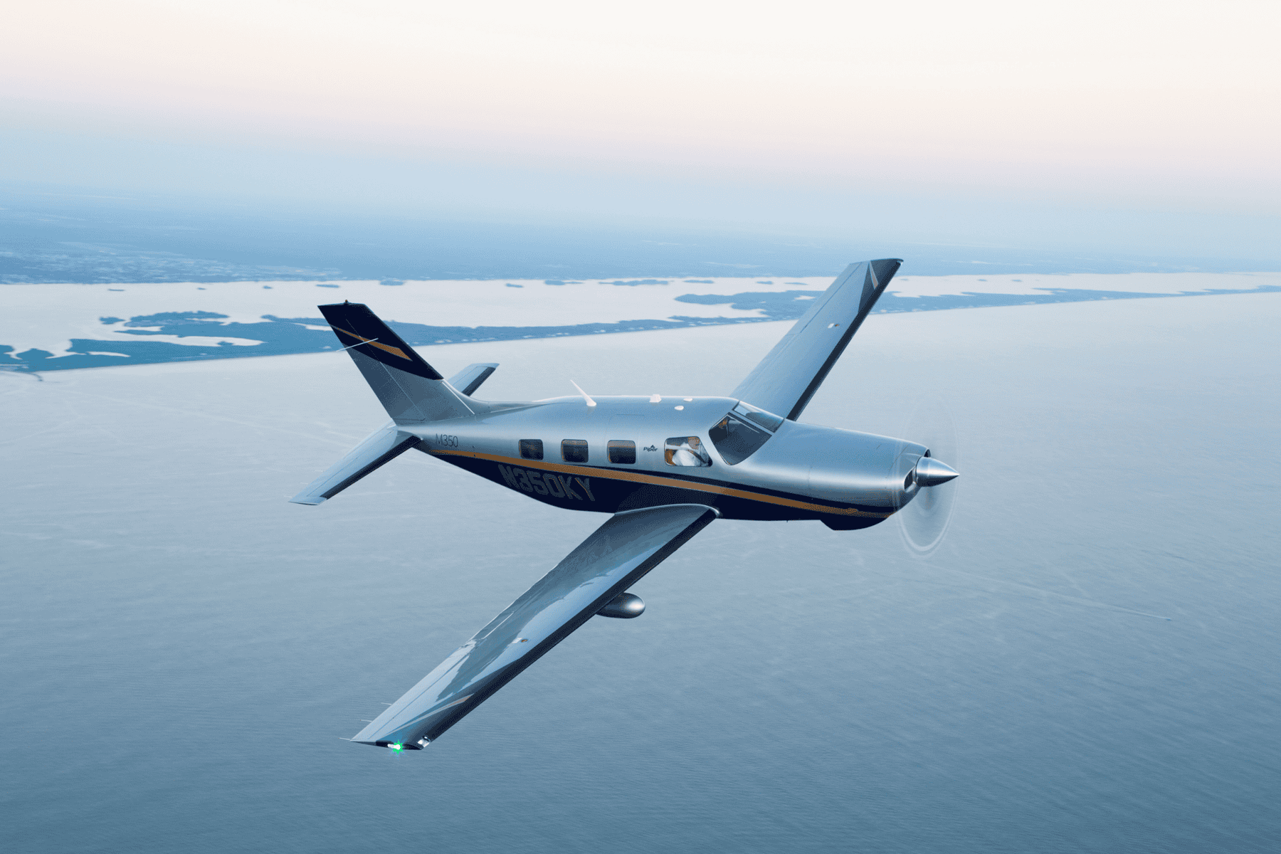 Small airplane flying over ocean at sunset.