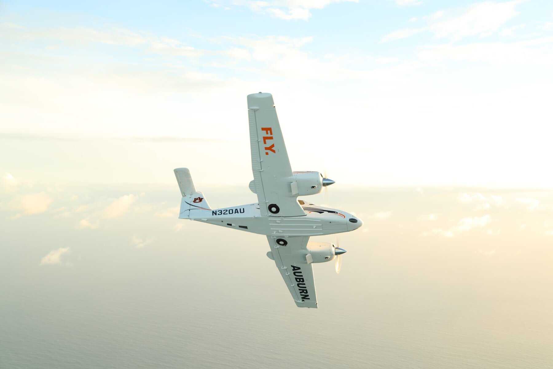 Small airplane flying over ocean at sunset.