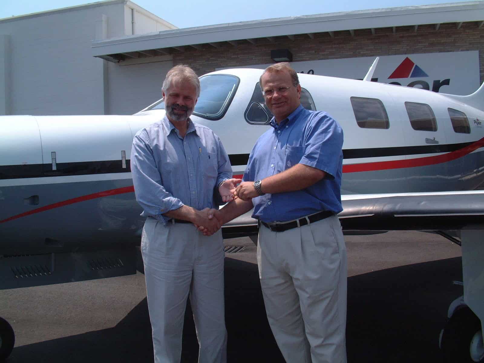 Two men shaking hands beside an airplane.
