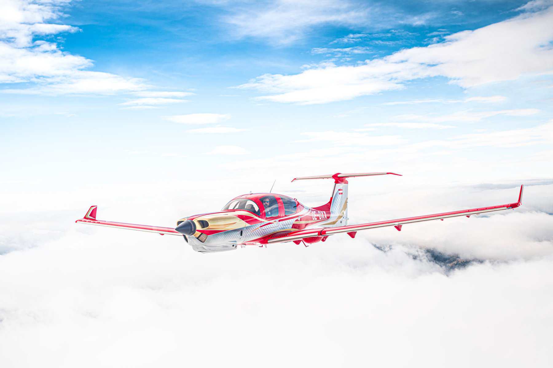 Red and white airplane flying above clouds